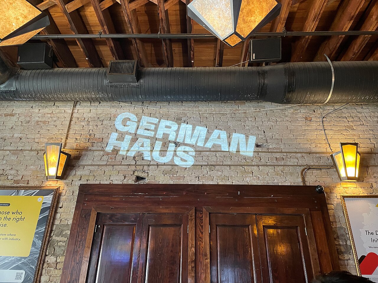 Innenansicht-German-Haus-SXSW.jpg Innenaufnahme des German Haus auf der SXSW in Austin, Texas, mit projiziertem Logo an der Backsteinwand und modernem Industrie-Look.