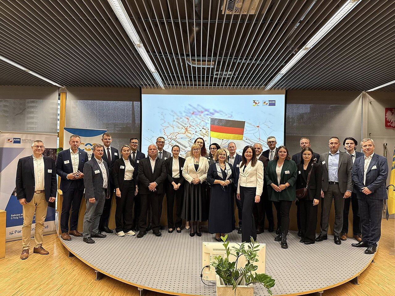 Gruppenfoto einer deutsch-polnischen Wirtschaftsdelegation bei einer AHK-Konferenz, mit Unternehmensvertretern und Partnern vor einer Präsentation mit Deutschland-Flagge